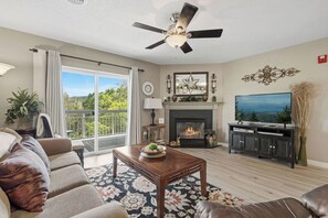 A living room with a fireplace, a television, and a ceiling fan.