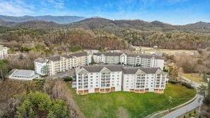 Ein mehrstöckiges Hotel mit Innenhof, umgeben von bewaldeter Landschaft und Bergen im Hintergrund.