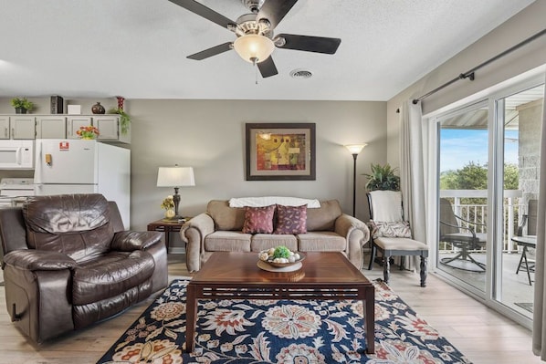 A living room with a ceiling fan, a sofa, a coffee table, and a view through a sliding glass door.