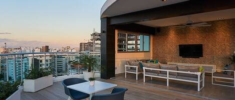 Un espacio exterior moderno con comedor, asientos y vistas a la ciudad.