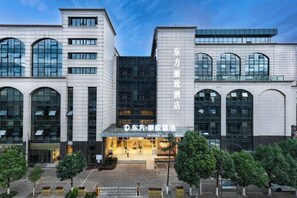 Ein modernes Hotel mit einem markanten Eingang, großen Fenstern und einem gepflegten Außenbereich mit Bäumen.