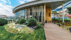 Un bâtiment moderne doté d’une façade en verre incurvé, d’une terrasse en bois et de jardins aménagés.