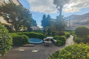 Une cour extérieure dotée d’une terrasse en bois, d’un espace salon circulaire et d’une végétation bien entretenue.
