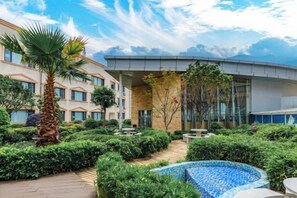 Une cour d’hôtel avec une piscine, des palmiers et un bâtiment moderne doté de grandes fenêtres.