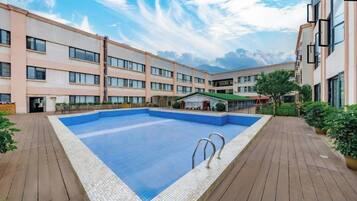 A swimming pool surrounded by a wooden deck, with a building featuring multiple windows and balconies in the background.