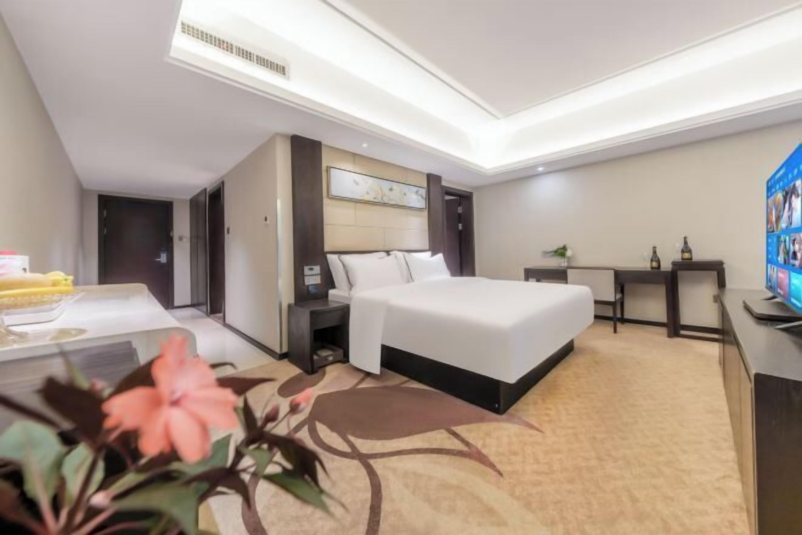 A hotel room with a bed, bedside table, nightstand, and a desk with a chair.