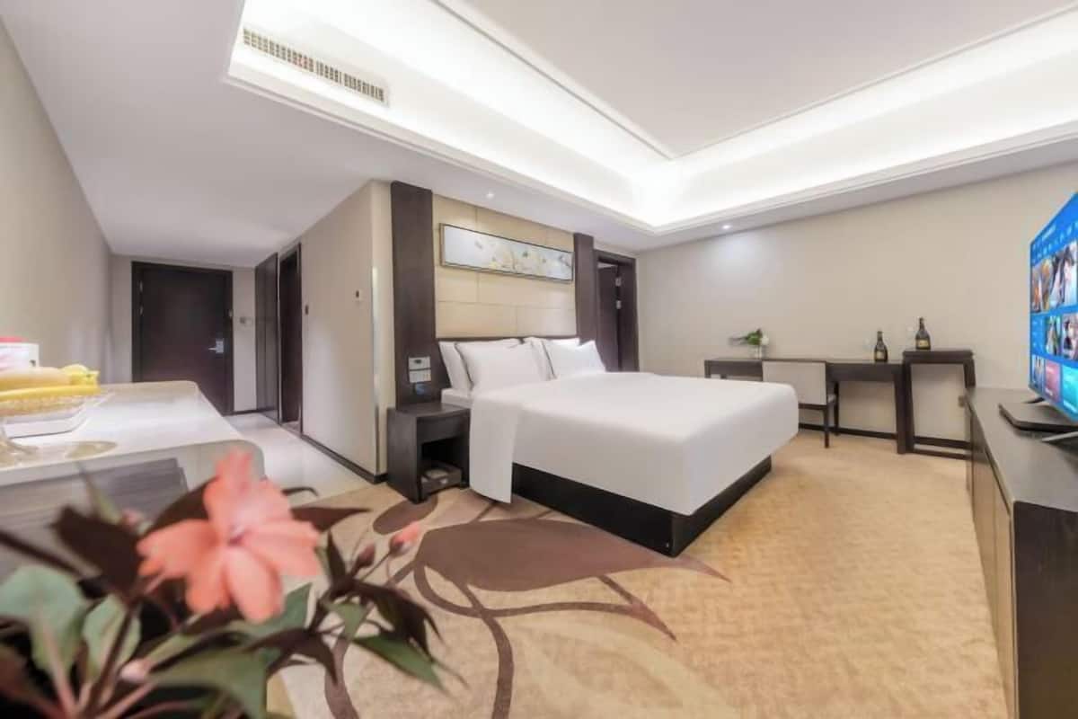 A hotel room with a bed, bedside table, nightstand, and a desk with a chair.