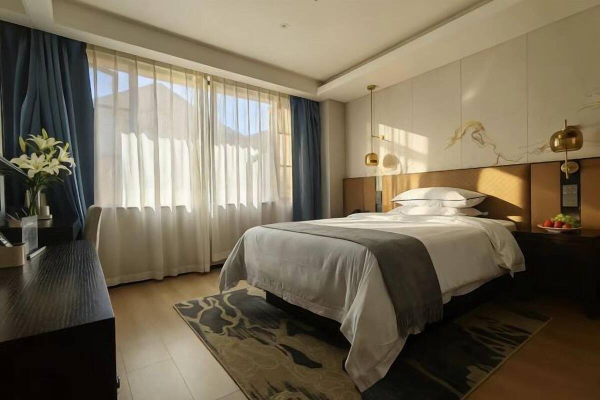 Una habitación de hotel moderna con una cama grande, un escritorio y un ventanal con cortinas translúcidas.