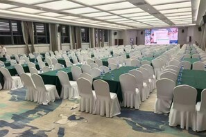 Une salle de conférence avec des rangées de tables et de chaises, de grandes fenêtres et un sol recouvert de moquette.