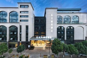 Un hôtel moderne doté d’une entrée centrale, de grandes fenêtres et d’un espace extérieur bien aménagé avec des arbres.