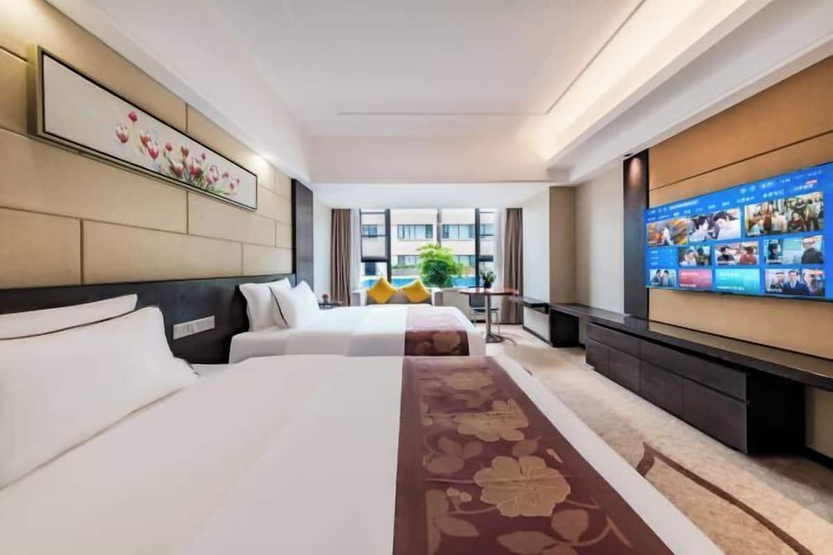 Habitación de hotel con dos camas, un televisor grande y vistas a la ciudad.