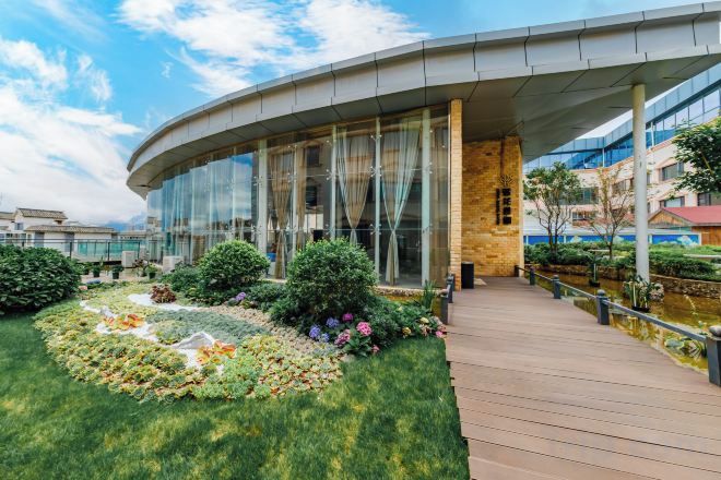 A modern building with a curved glass facade, a wooden deck, and a landscaped garden area.