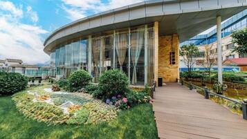 A modern building with a curved glass facade, a wooden deck, and a landscaped garden area.