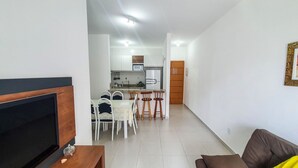 A living room with a TV, a brown sofa, and a dining area with a table and chairs. - Apartment Praia Grande Ubatuba | REF KC04H (Ubatuba)