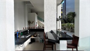 A modern kitchen with a black countertop, wooden chairs, and a staircase leading to an upper level. - Apartment Praia Grande Ubatuba | REF KC04H (Ubatuba)
