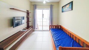 Una habitación con televisión, estanterías de madera, un colchón azul y un cuadro en la pared.