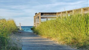 A wooden boardwalk leading to a beach house with a view of the ocean.