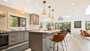A modern kitchen with a central island, bar stools, and large windows.