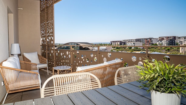 A balcony with wicker furniture, a potted plant, and a view of buildings in the distance.