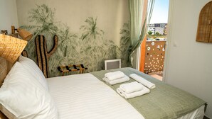 A hotel room with a bed, a cactus decoration, a view of the city through a window, and a green curtain.