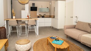 A modern living room with a sofa, a coffee table, and a dining area with chairs and a kitchen in the background.