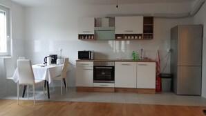 Une cuisine moderne avec des meubles blancs, un four à micro-ondes, un évier et un réfrigérateur. On y trouve une table à manger avec des chaises, ainsi qu’une fenêtre qui laisse entrer la lumière naturelle.