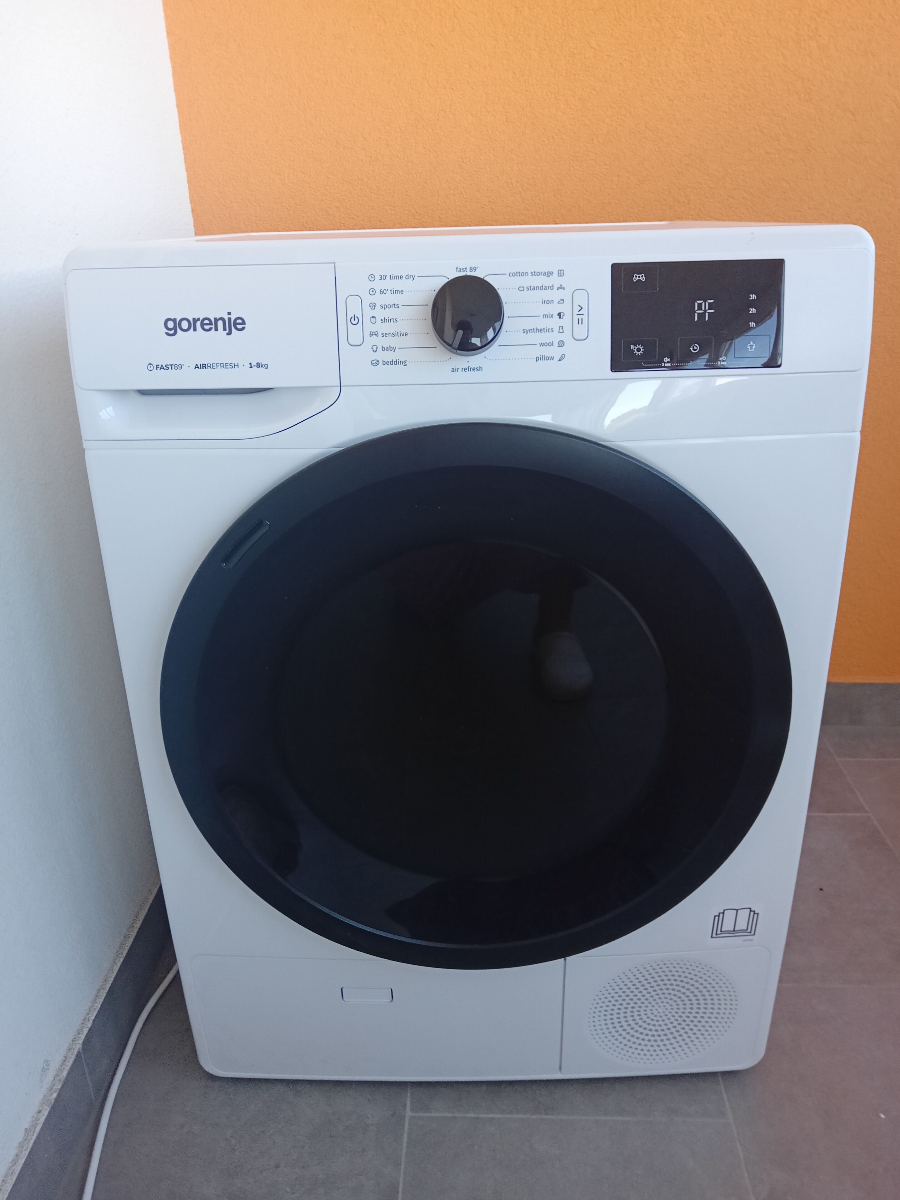 Una lavadora blanca con un panel de control, una puerta negra y una pantalla digital.