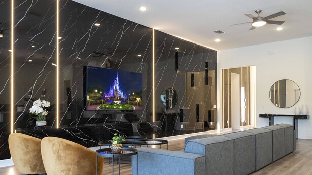 Ein modernes Wohnzimmer mit großem Flachbildfernseher, einem grauen Sofa, zwei Sesseln und einem Couchtisch.