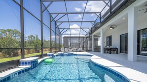 Ein Schwimmbad mit Glasveranda, umgeben von einer Terrasse mit Gartenmöbeln.