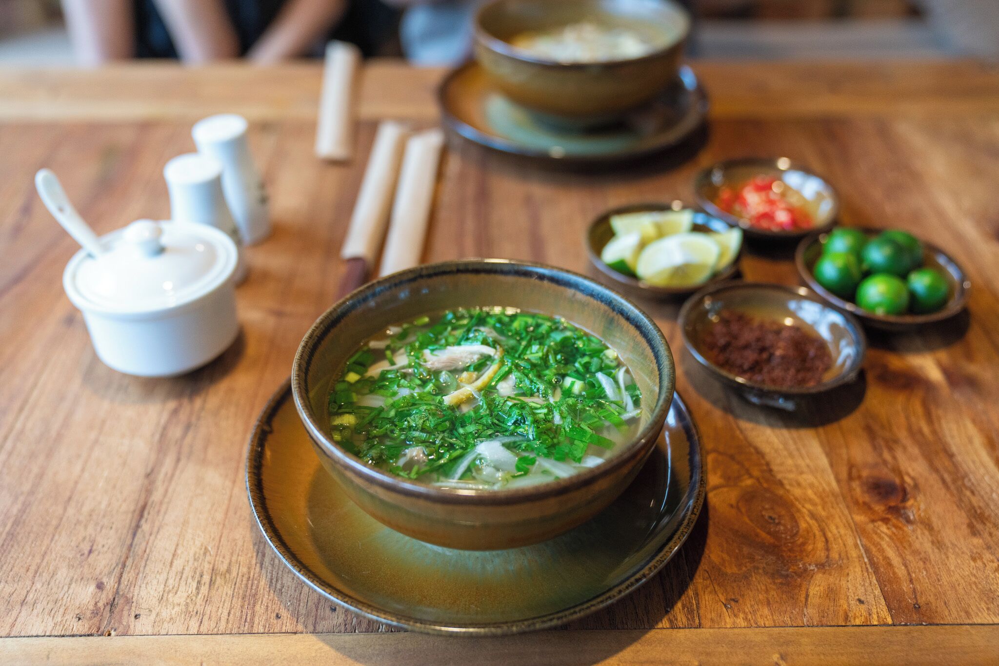 Una mesa con un tazón de sopa, salsas y una cuchara.