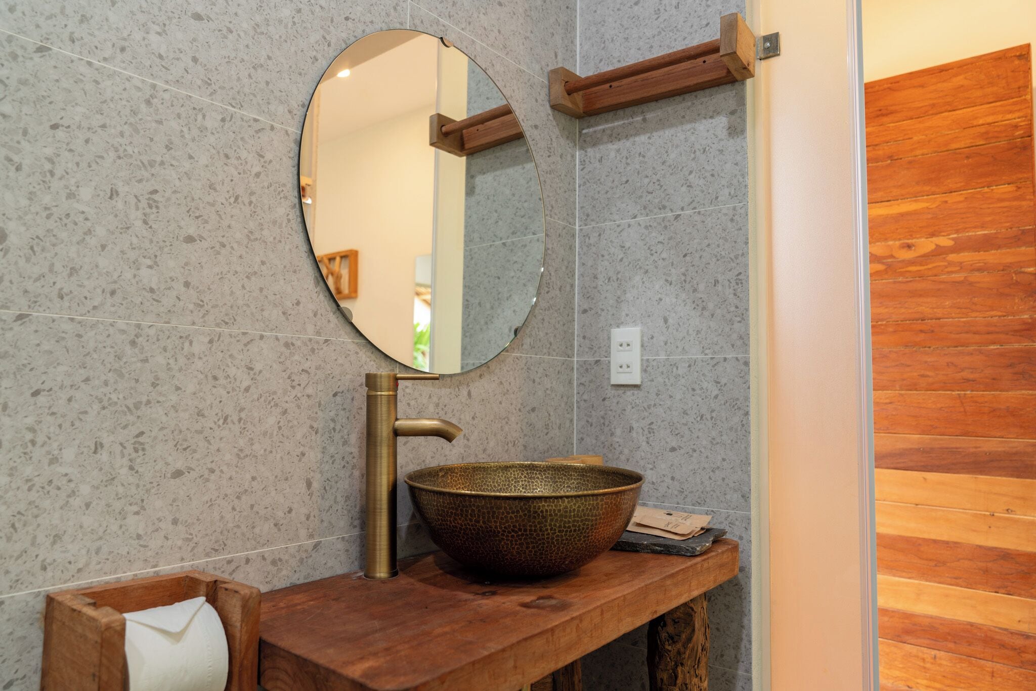 A bathroom with a round mirror, a wooden vanity, and a large ceramic basin.