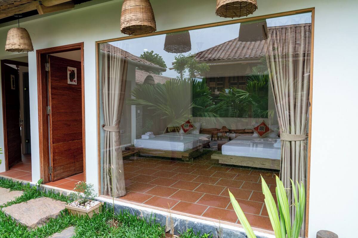 Ein traditionell eingerichtetes Schlafzimmer mit zwei Betten, einem großen Fenster mit Vorhängen und einem kleinen Balkon.