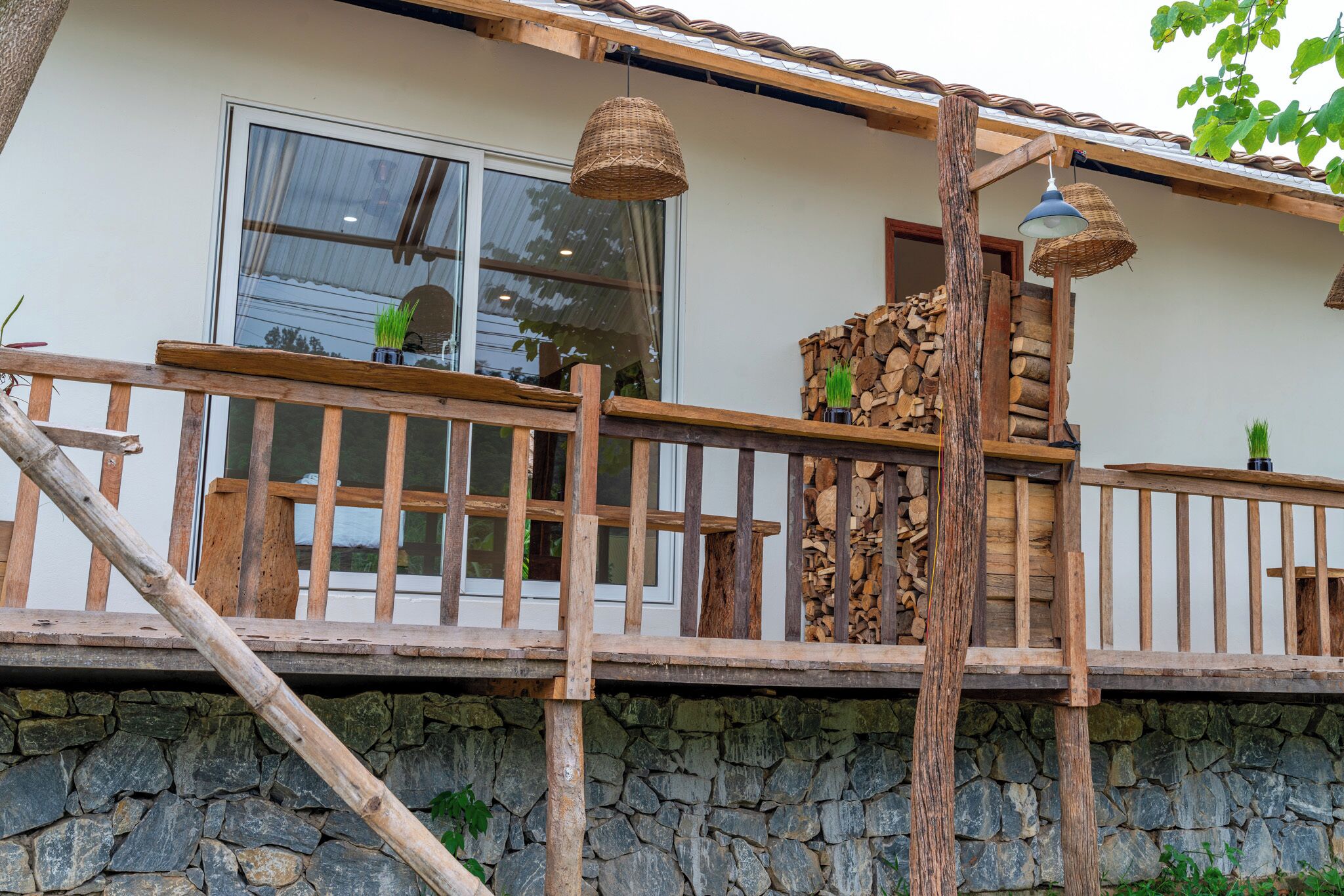 A wooden deck with a stone wall, a wooden railing, and a window with a curtain.
