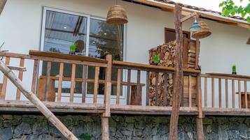 A wooden deck with a stone wall, a wooden railing, and a window with a curtain.