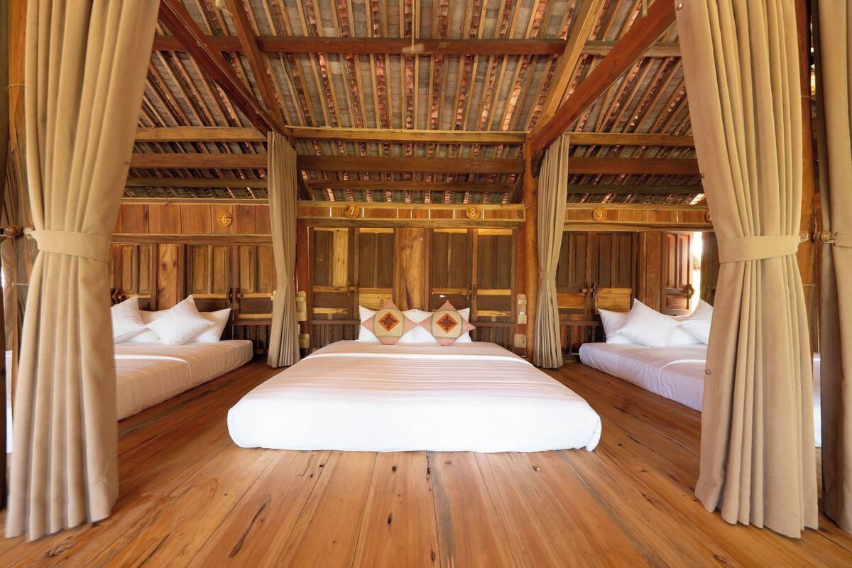 Ein geräumiges Zimmer mit einem großen Bett, zwei kleineren Betten, Holzwänden und einer hohen Decke.