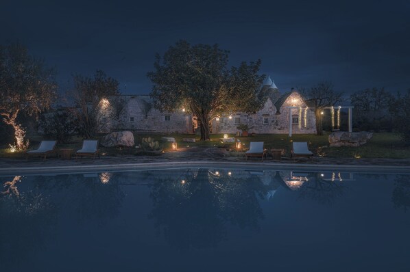 A stone building with a pool, lounge chairs, and string lights. - La Casedda don Gaetano: nature and pool in the trulli village (Monopoli)