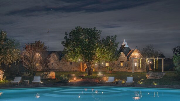 Un bâtiment en pierre doté d’une piscine, de chaises longues et de guirlandes lumineuses.