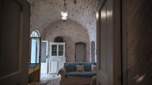 Une pièce avec un plafond en pierre, un meuble blanc aux portes vitrées, un canapé bleu avec des coussins et un tapis à motifs sur le sol.