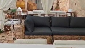 Un espace extérieur aménagé avec un canapé en osier, une table blanche et un saladier rempli d’œufs.