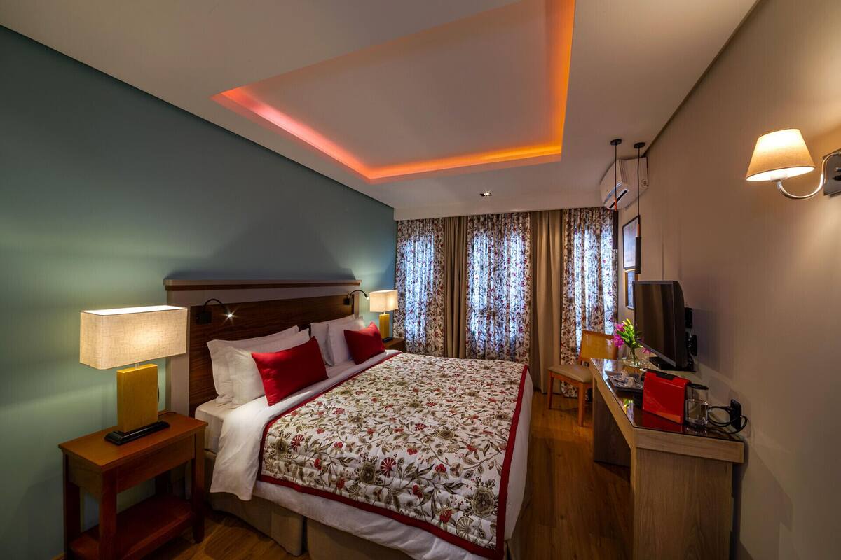A hotel room with a bed, bedside lamps, a desk with a TV, and curtains.