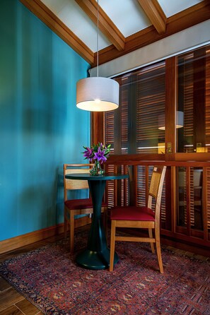 A room with a wooden ceiling, a table with a vase of flowers, a chair, and a patterned rug. - Hotel Boutique Britânico (Gramado)