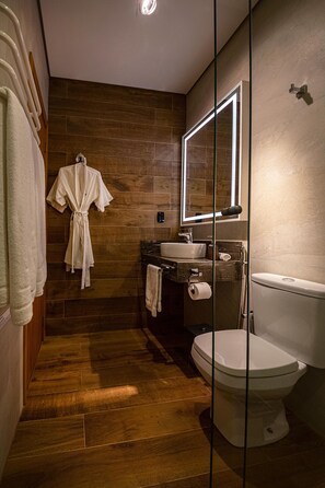 A modern bathroom with wooden flooring, a white sink, a toilet, and a robe hanging on the wall. - Hotel Boutique Britânico (Gramado)