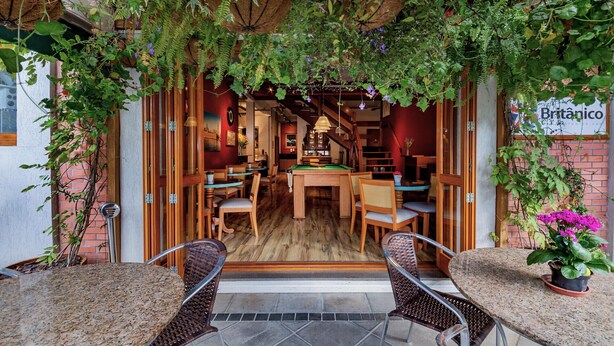 A cozy indoor seating area with wooden tables and chairs, a billiards table, and a brick wall. - Hotel Boutique Britânico (Gramado)