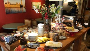 A buffet setup with various food items, including fruits, vegetables, and desserts, arranged on a wooden table. - Hotel Boutique Britânico (Gramado)