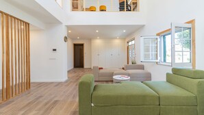 A spacious living area with a high ceiling, a wooden partition, a sofa set, and a window with a view.
