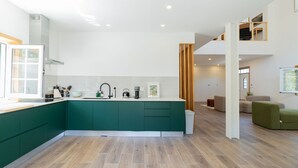 A modern kitchen with a central island, a dining area with a sofa, and a staircase leading to an upper level.