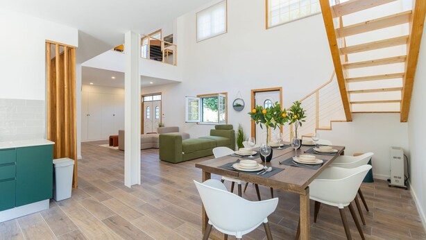 A spacious living area with a dining table set for four, a green sofa, and a staircase leading to an upper level.