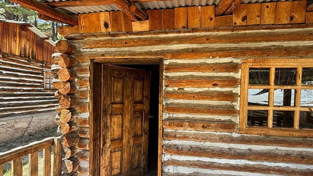 A log cabin with a wooden door and window, a stone floor, and a metal roof. - CABAÑAS BATOSARACHI (Bocoyna)