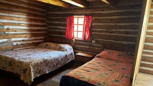 A log cabin room with two beds, wooden floors, a window with red curtains, and a wooden headboard. - CABAÑAS BATOSARACHI (Bocoyna)