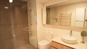 Un baño moderno con ducha de vidrio, inodoro y tocador con lavamanos y espejo.